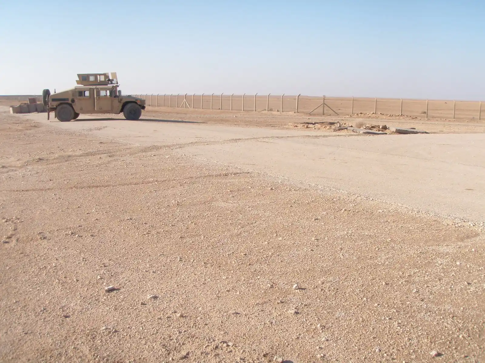 A Humvee parked beside a perimeter fence on the open desert at Al Asad, Iraq.
