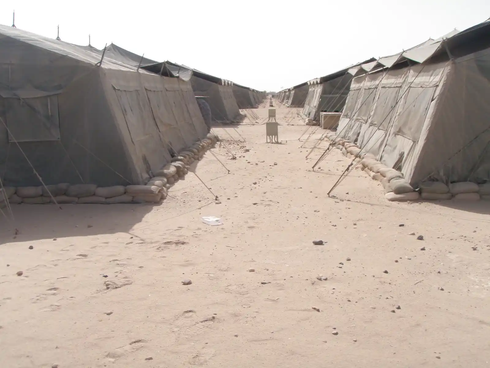 A sandy walkway running between two long rows of military tents at a camp in Kuwait.